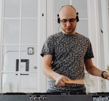 Bald man using electronic mallet percussion instrument with headphones at home.