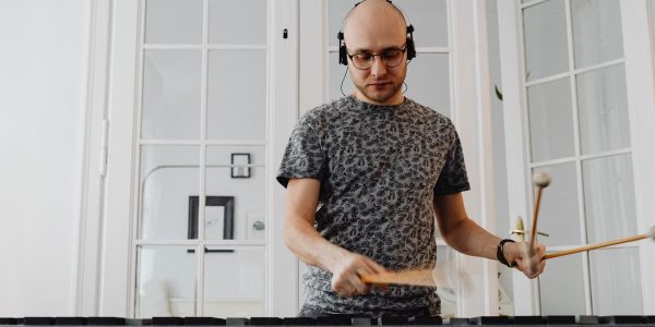 Bald man using electronic mallet percussion instrument with headphones at home.