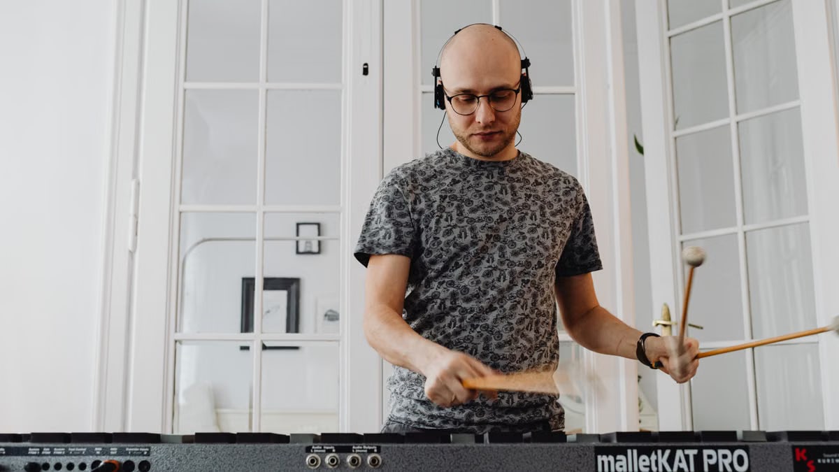 Bald man using electronic mallet percussion instrument with headphones at home.